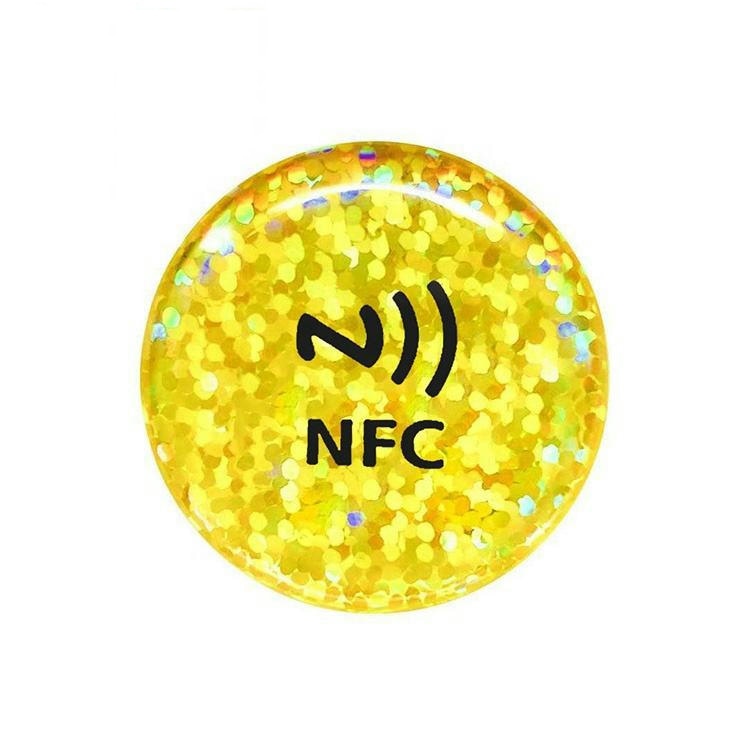 Zlatna okrugla ispupčena NFC nalepnica od epoksidne smole visokog nivoa zaštite sa šljokicama i NFC oznakom služi za potvrdu autentičnosti i promociju premijum brenda.