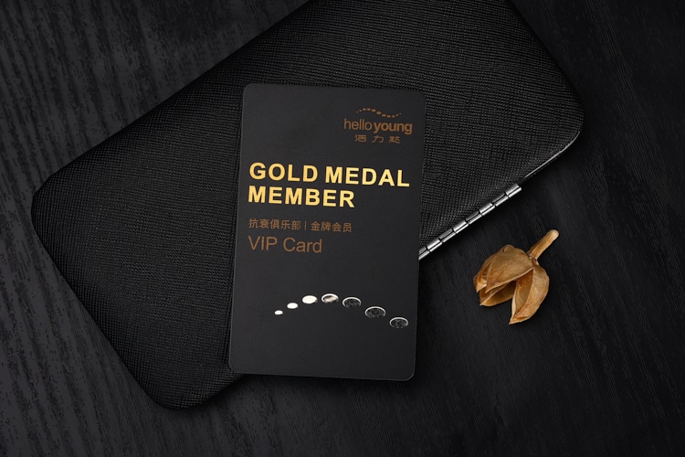 Crna plastična VIP kartica sa tekstom zlatni medaljon član i uzorkom kapljica prikazana na tamnoj površini stola za elitne programe lojalnosti.