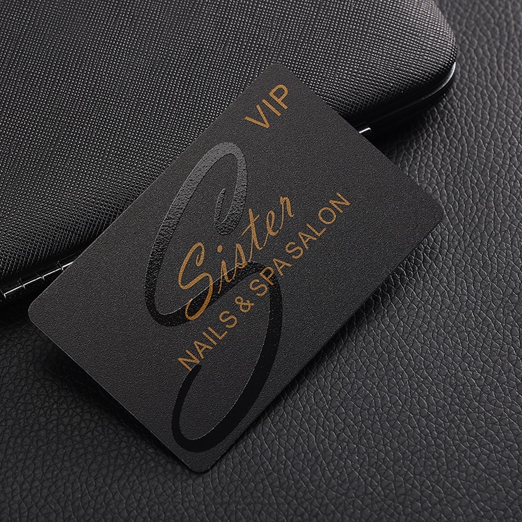 Mat crna VIP plastična kartica sa velikim logotipom ispisanim rukopisom i zlatnim tekstom prikazana na koži kako bi se dočarala elegantna završna obrada brenda.