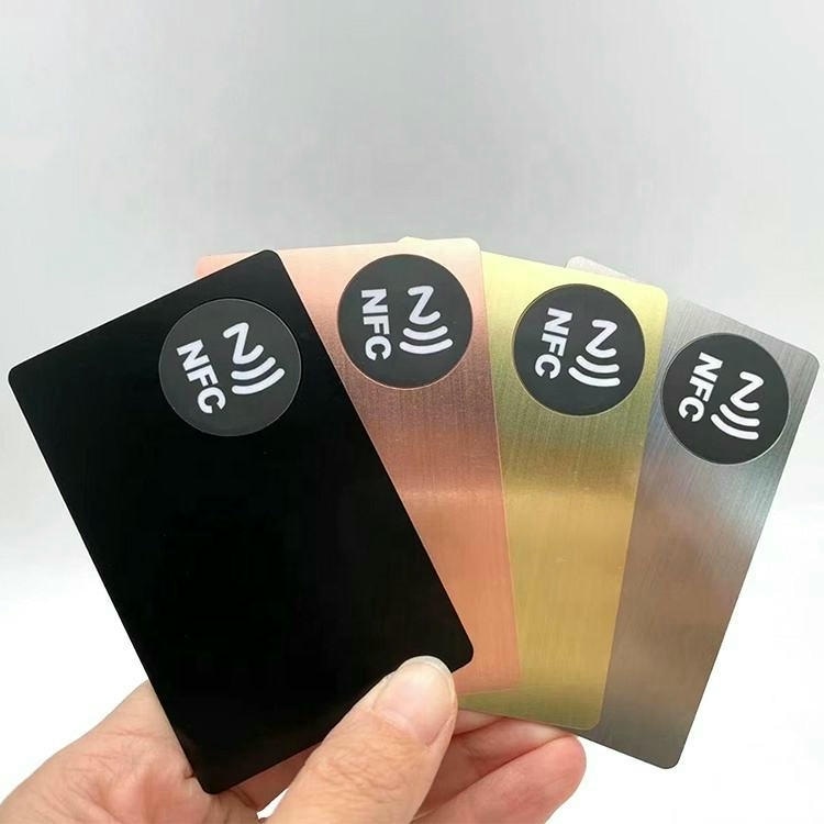 Četiri metalne vizitkarte u crnoj bakarnoj zlatnoj i srebrnoj boji prikazuju NFC ikone za beskontaktni rad i integraciju pametne kartice u metal.