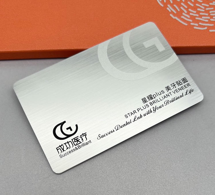 Brušena srebrna plastična kartica sa prozirnim logotipom prikazuje brendiranje stomatološke laboratorije i motivacioni tekst na premijum teksturiranoj završnoj obradi.