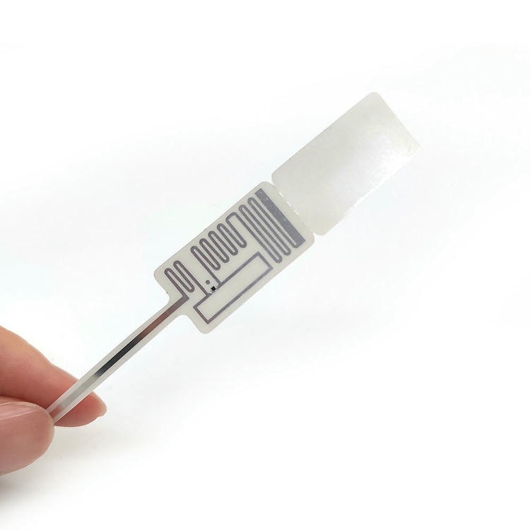 Jedna RFID oznaka za nakit drži se u ruci kako bi se prikazali prednja površina za štampanje i otkriven raspored antene.
