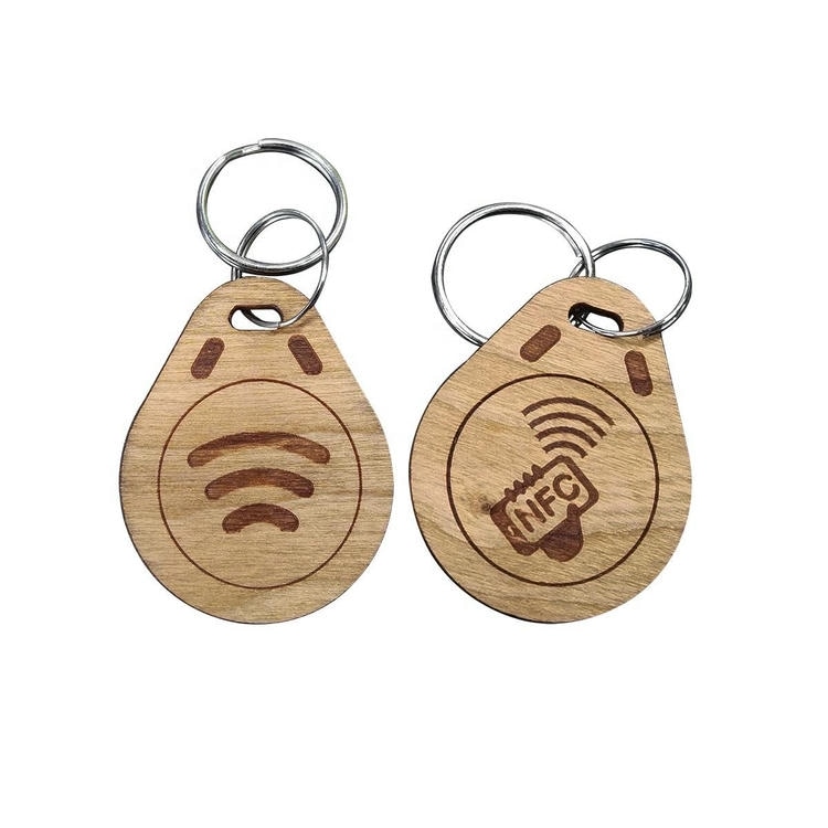 Par drvenih RFID privezaka u obliku kapi sa alkama od nerđajućeg čelika ima laserski graviran WiFi simbol i NFC oznaku na prirodnoj teksturi drveta.