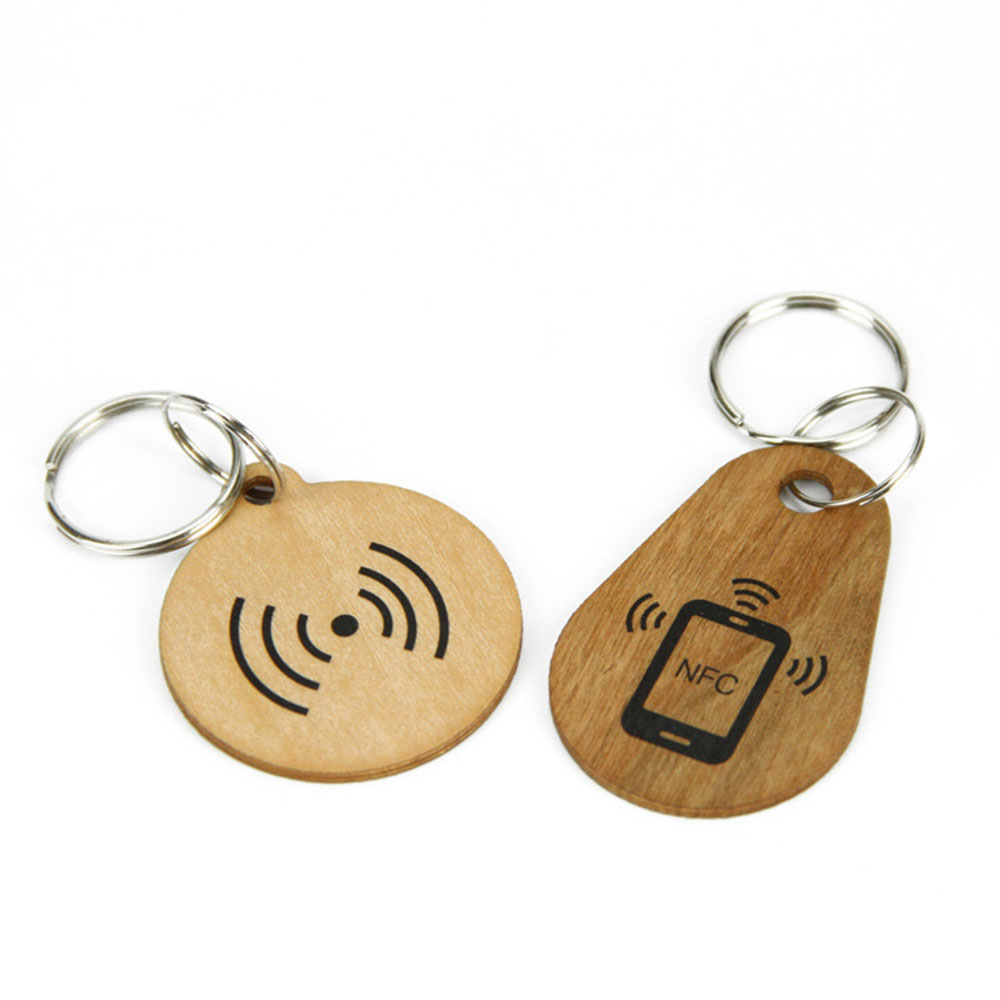 Dva drvena RFID privitka za ključeve na beloj pozadini prikazuju klasičnu okruglu pločicu sa talasom u paru sa pločicom u obliku suze sa NFC ikonom na prstenovima.