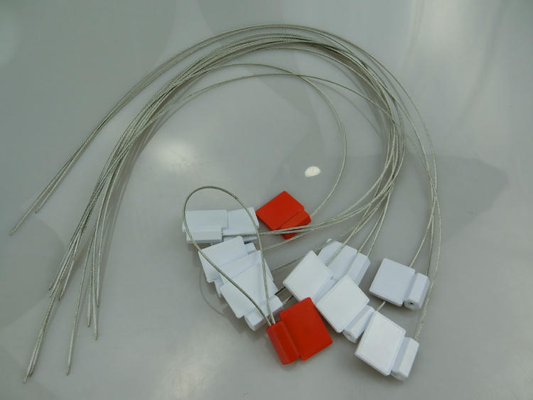 Bele i crvene SS3626-1 RFID sigurnosne plombe su grupisane zajedno sa dugim labavim čeličnim žicama na sjajnoj površini.
