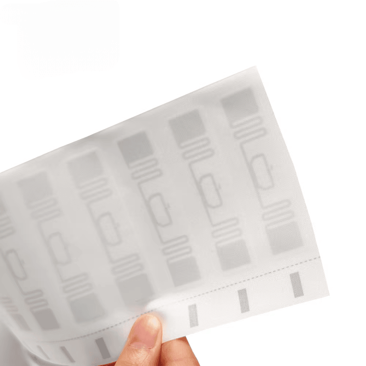 Ruka pridržava belu RFID tekstilnu etiketu radi prikaza ponovljenog rasporeda tkanog inlaja na više pozicija na etiketi.
