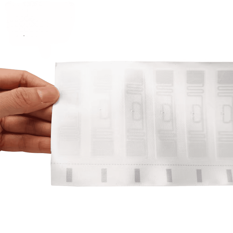 Široki prikaz iz ruke predstavlja tabak bele RFID tekstilne etikete sa više integrisanih UHF inlaja raspoređenih po tkanini.