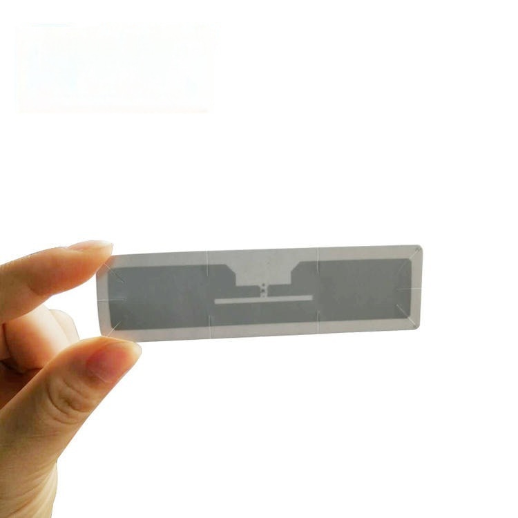 Ruka drži tanak UHF RFID inlej za vetrobransko staklo na beloj pozadini, prikazujući nagraviranu antenu za pristup naplatnim rampama.
