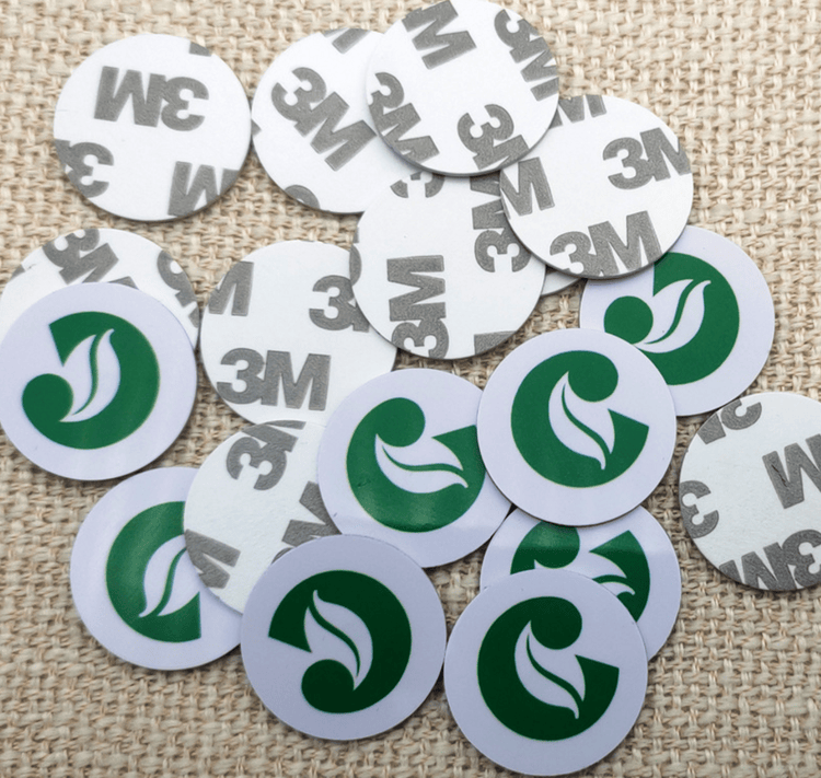 Grupa iz blizine PVC RFID okruglih tagova sa štampanim zelenim simbolom i vidljivim krugovima lepljive podloge na površini od jute.