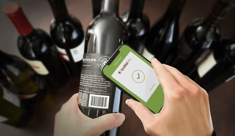 Na ovoj slici je prikazana ruka koja skenira flašu vina pametnim telefonom radi provere statusa pakovanja putem platforme povezane sa RFID-om.