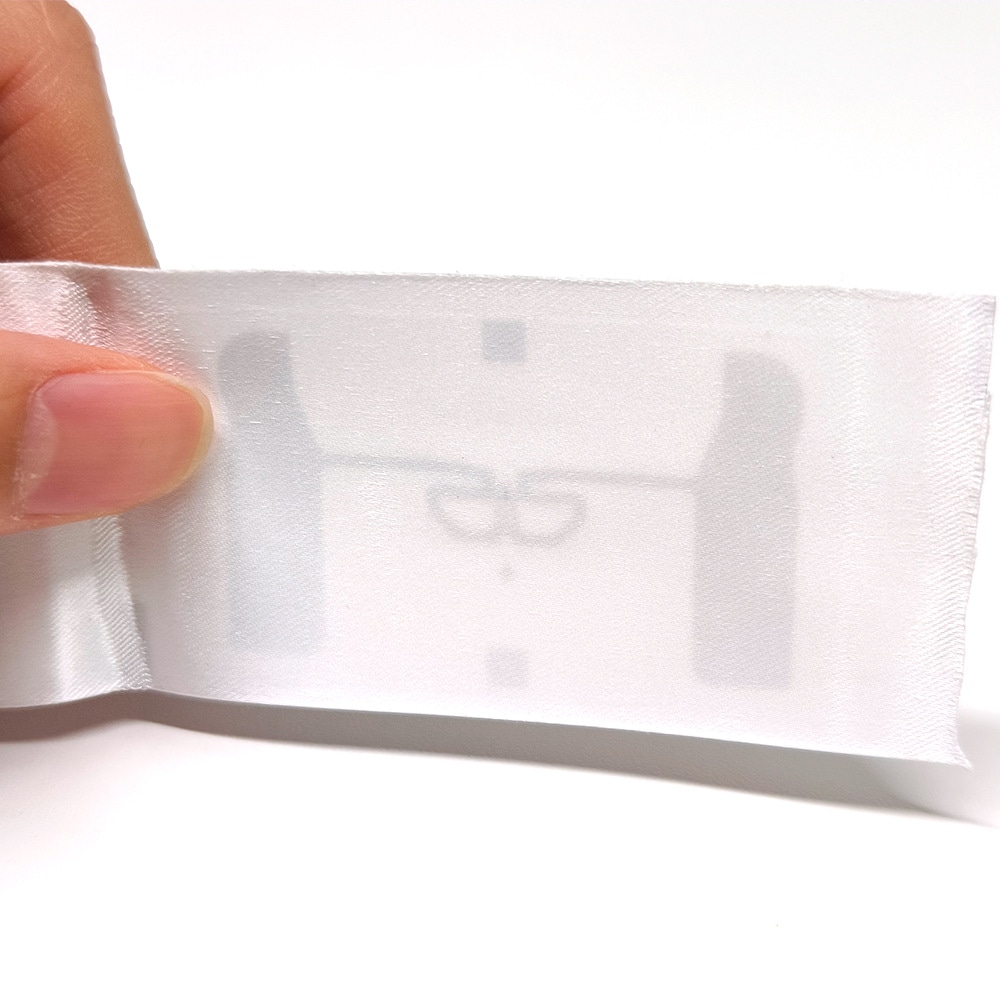 Krupni prikaz kompaktne RFID oznake za odeću pokazuje poluprovidan tkani materijal etikete i središnji obrazac antene za upotrebu u perionicama.