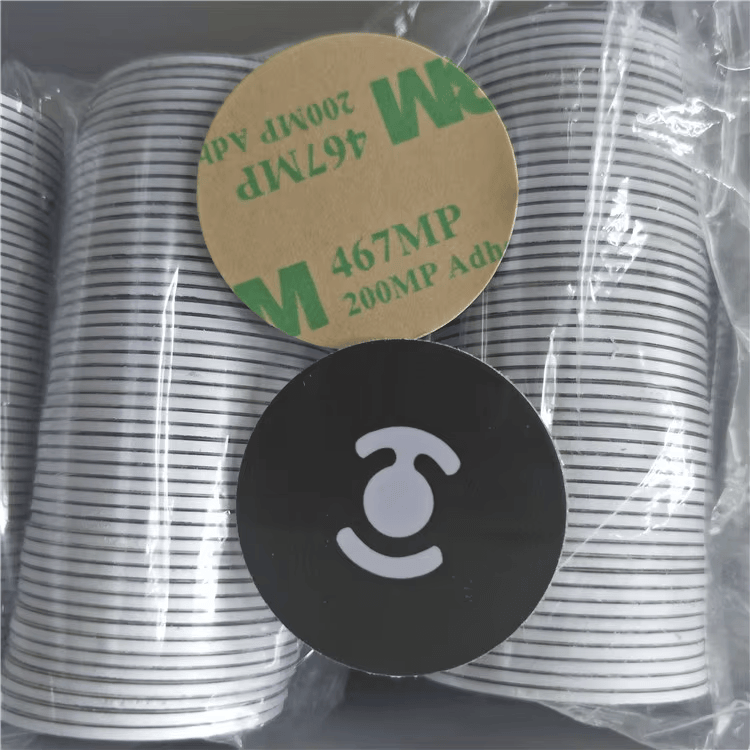Detaljan prikaz upakovanih RFID disk tagova prikazuje disk sa lepljivom podlogom iznad crnog diska sa logotipom unutar zaštitne plastike.