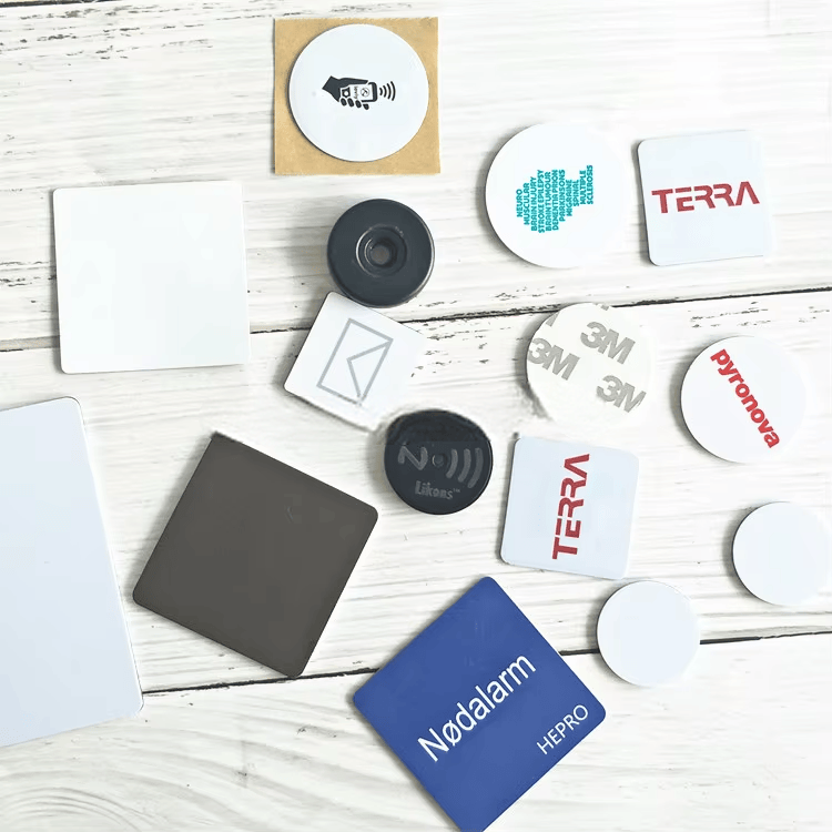 Više uzoraka PVC RFID oznaka u obliku novčića raspoređeno je po stolu i prikazuje različite veličine štampu i vrste poleđine.