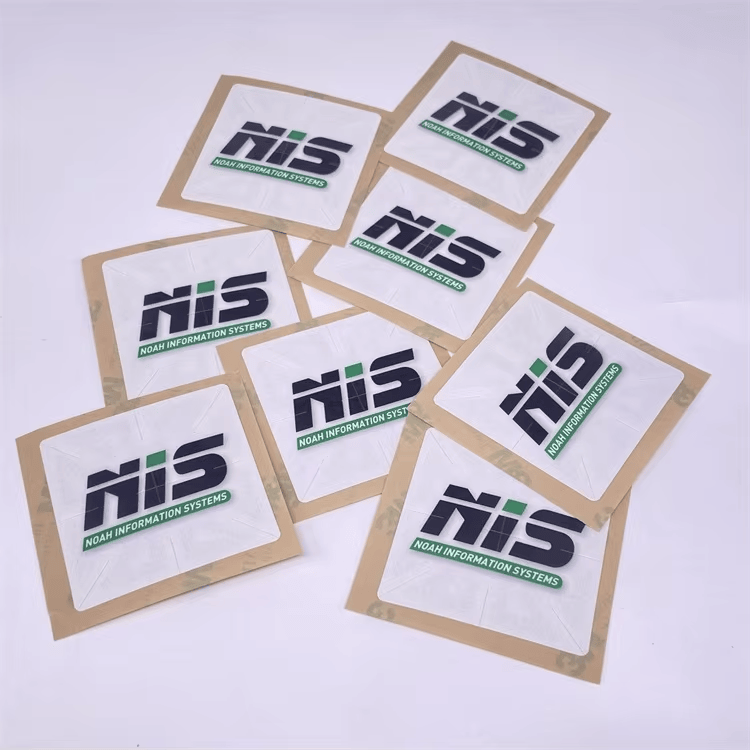 Više kvadratnih RFID registracionih nalepnica za vetrobran raspoređeno je na stolu s ujednačenim brendiranjem NIS za upotrebu u voznom parku.
