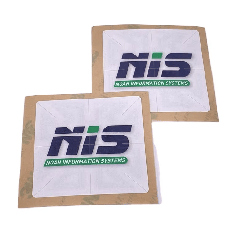 Dve kvadratne RFID registracione nalepnice za vetrobran naslagane su na zaštitnom papiru s izdignutim logotipom NIS i spremne za postavljanje na vetrobran.