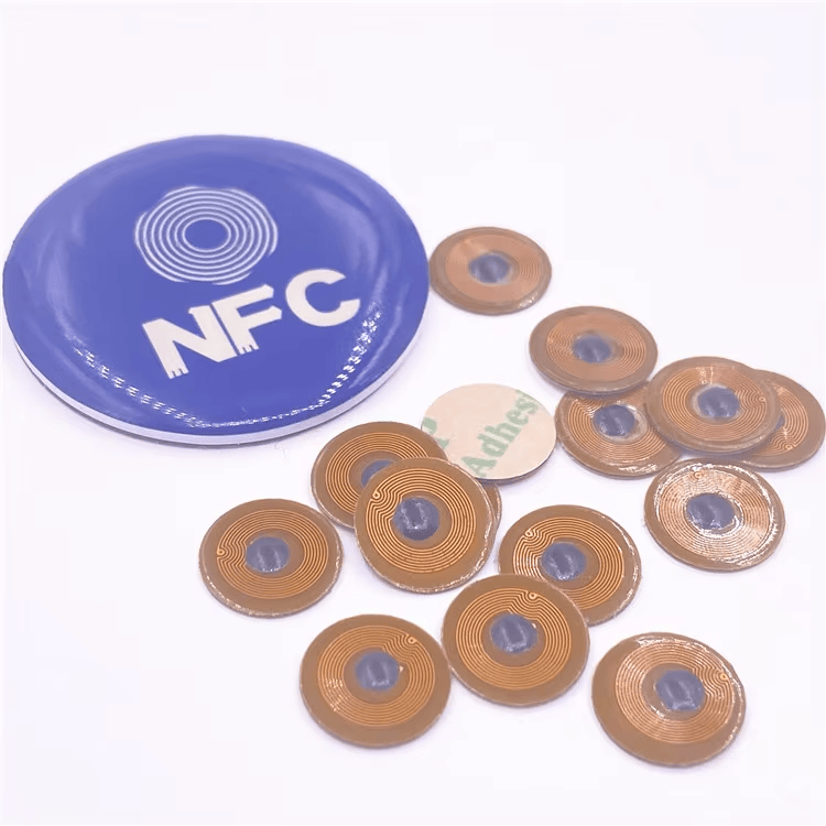 Mikro NFC oznake FPC10-1 fotografisane su pored diska s NFC simbolom kao pokazatelj da ih pametni telefon može očitavati na metalnim površinama.