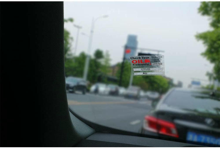 Pogled iz unutrašnjosti automobila pokazuje statičku RFID nalepnicu za podsećanje o zameni ulja na vetrobranskom staklu, pričvršćenu na staklo ispred.