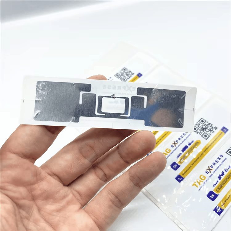 Poleđina sa antenskim inlejom UHF RFID nalepnice za pristup kroz vetrobransko staklo prikazana je u ruci radi objašnjenja postavljanja inleja unutar taga.
