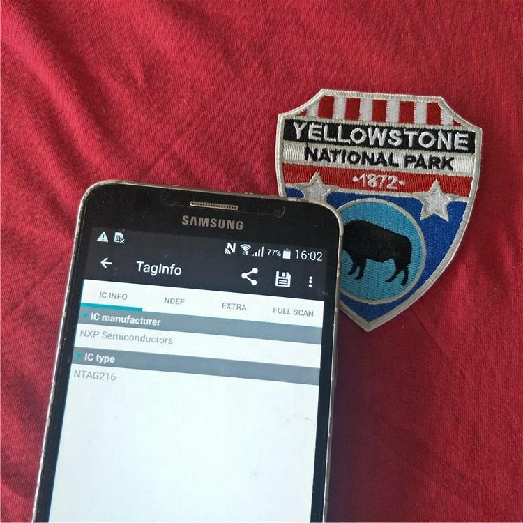 Izbliza snimljena pametna NFC etiketa ugrađena u jaknu za spoljnu upotrebu koju mobilni telefon čita radi autentifikacije.