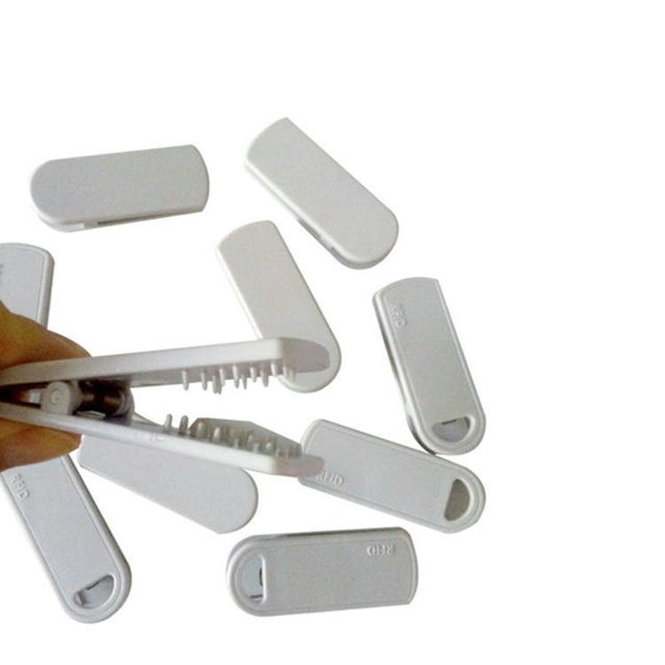 Ova slika prikazuje ruku koja otvara SV-014 RFID clip tag dok je nekoliko tela tagova razbacano oko proizvoda.