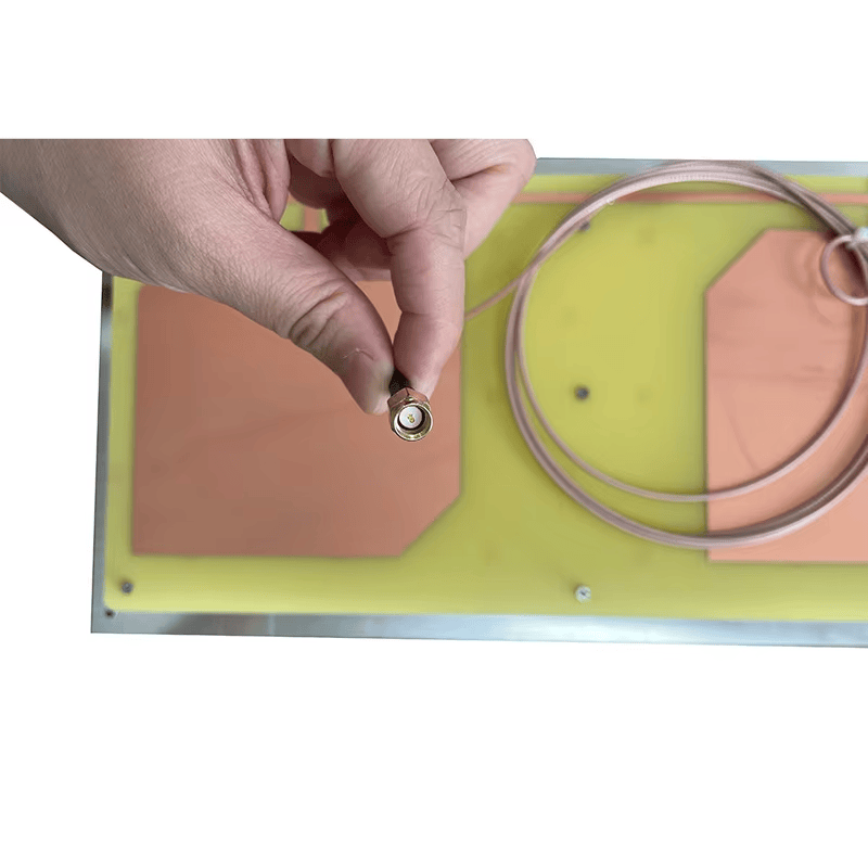 Slika prikazuje ruku koja drži kabl sa SMA priključkom UHF RFID antene uskog snopa ZK-ANT9021 iznad tela antene.