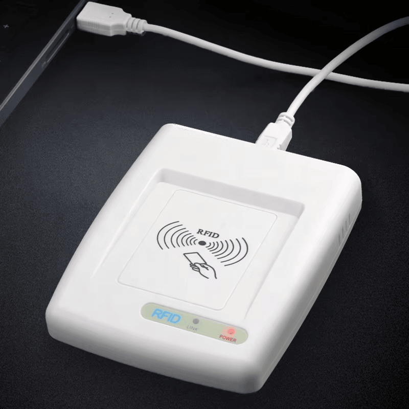 Ova fotografija prikazuje HF RFID čitač RC200U povezan USB kablom na stolu radi demonstracije rada uz napajanje i prenosa podataka.