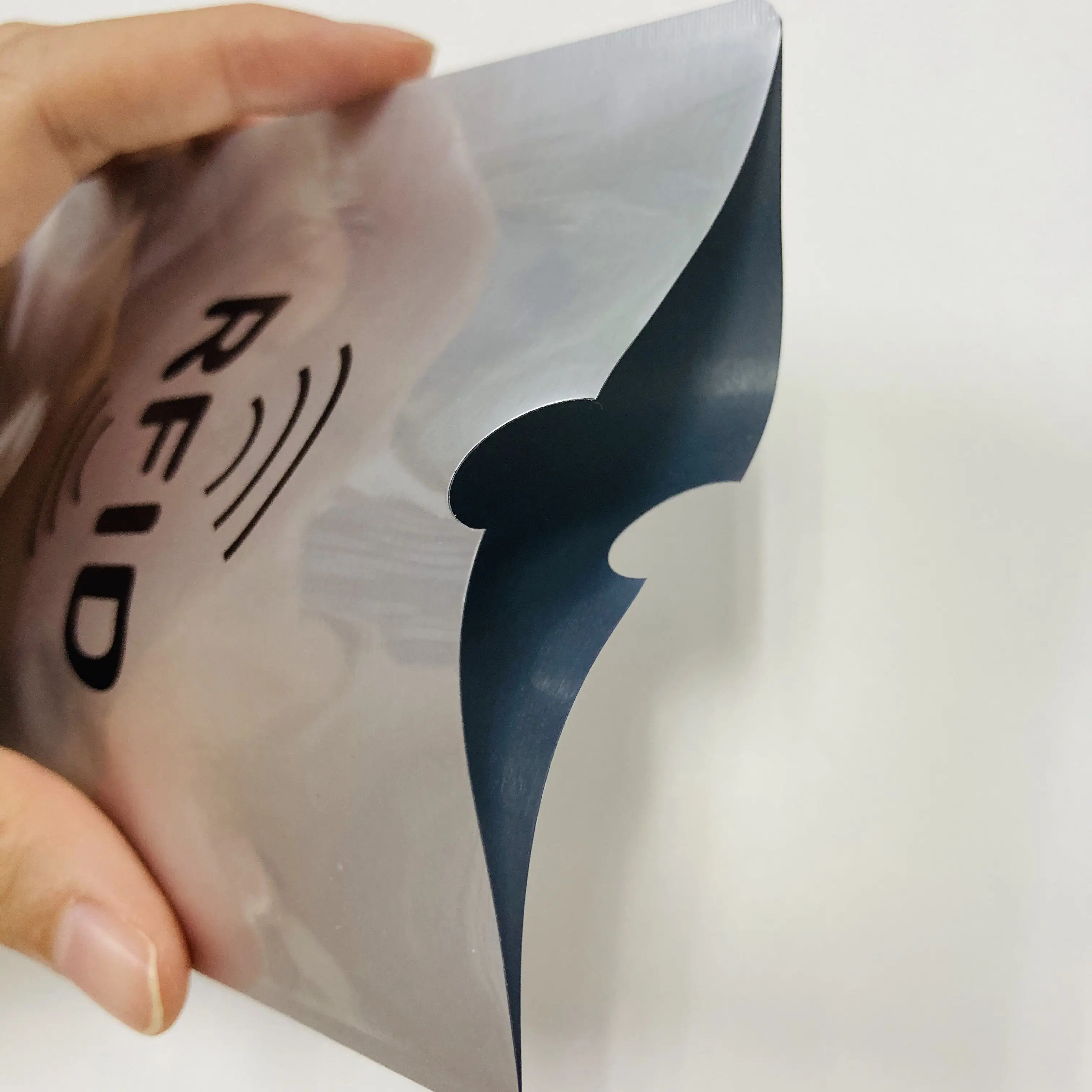 Srebrna RFID zaštitna futrola je stisnuta i otvorena blizu zareza, otkrivajući tamni unutrašnji sloj koji pomaže u blokiranju beskontaktnih signala.