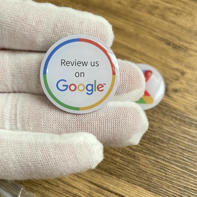 Ruka u rukavici drži NFC nalepnicu od epoksidne smole u obliku po meri sa belom oznakom za Google recenziju koja podržava beskontaktno aktiviranje dodirom.